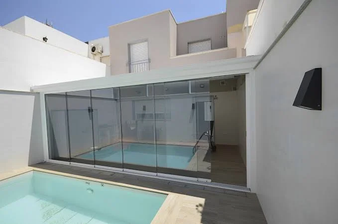 Patio de una vivienda con una habitación acristalada y una piscina en primer término