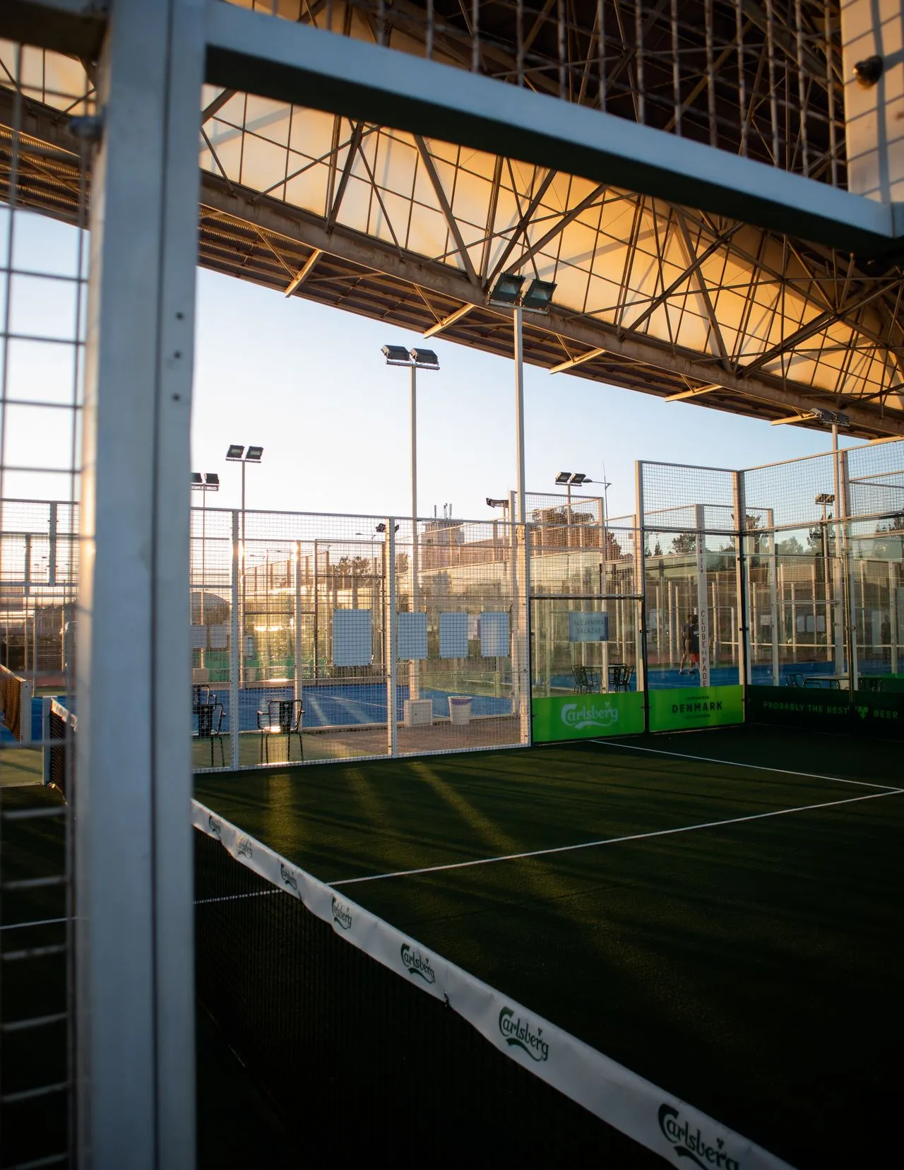 Pistas de pádel con cerramiento de cristal y malla en un club deportivo al atardecer